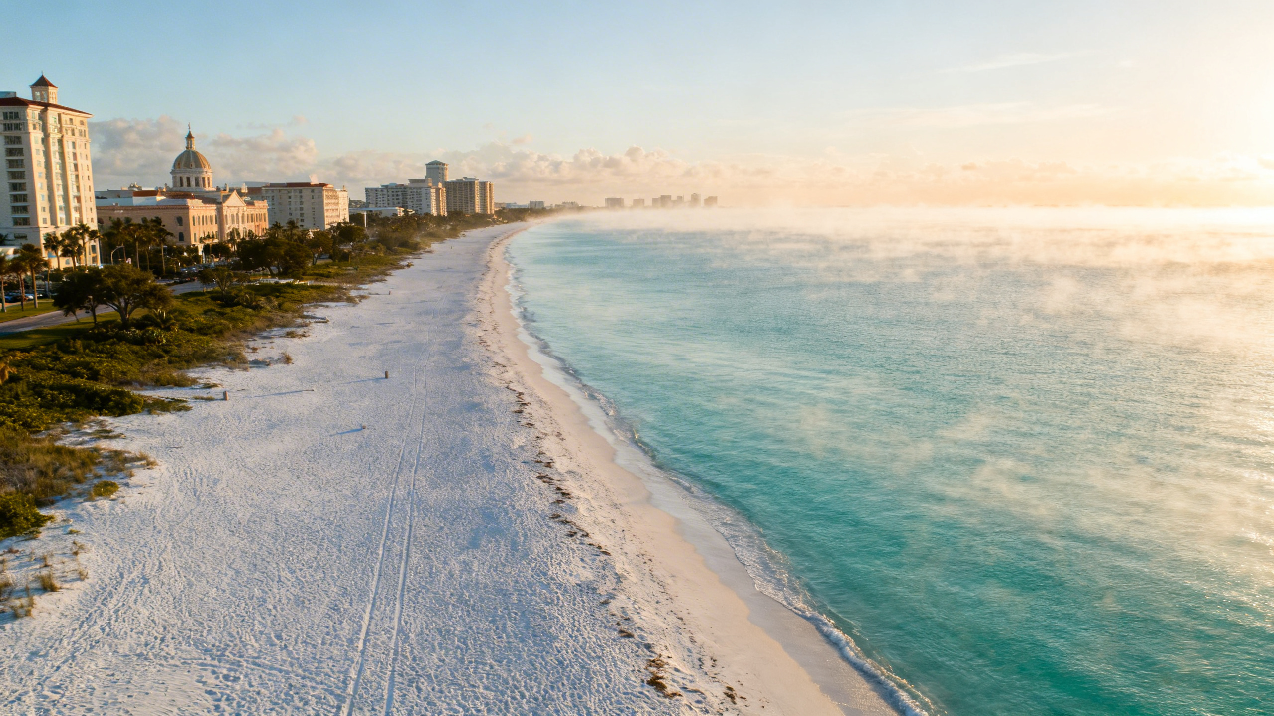 White sandy beaches and turquoise waters stretching along Sarasota coastline under a sunny late afternoon sky