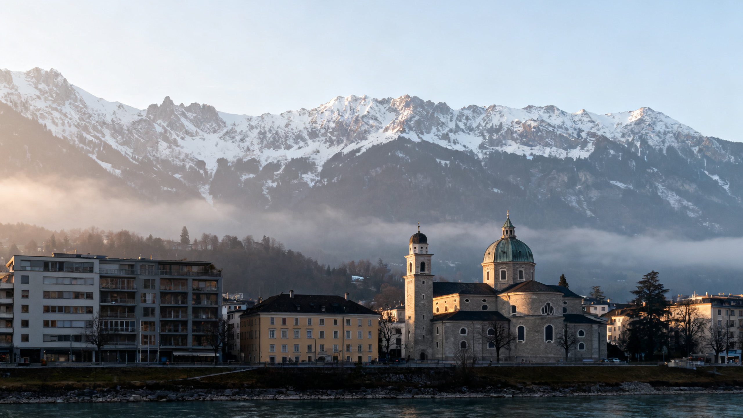 Snow-capped mountains overseeing a small city with both modern and historic buildings in late afternoon light