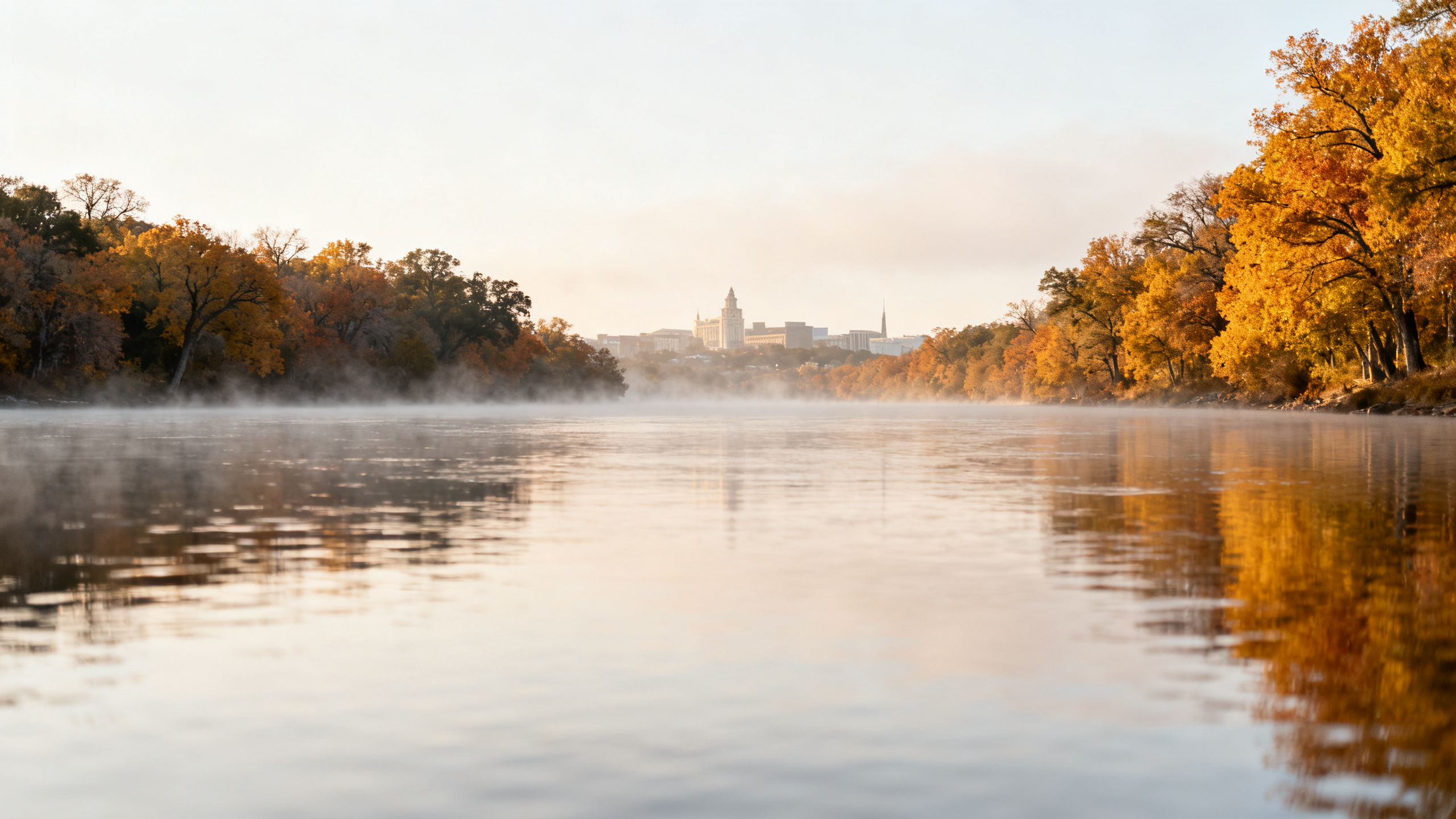 A tranquil stretch of the Colorado River near Bastrop, lined with trees showing fall colors under soft afternoon light.