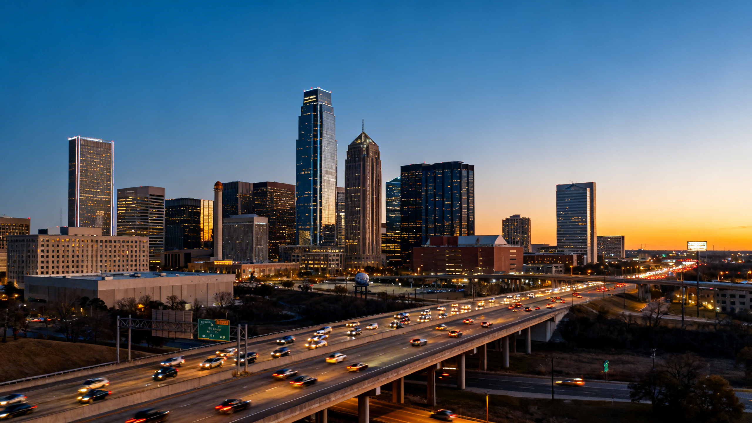 Skyline of Dallas with modern office towers and highway flooding with traffic during golden hour light.