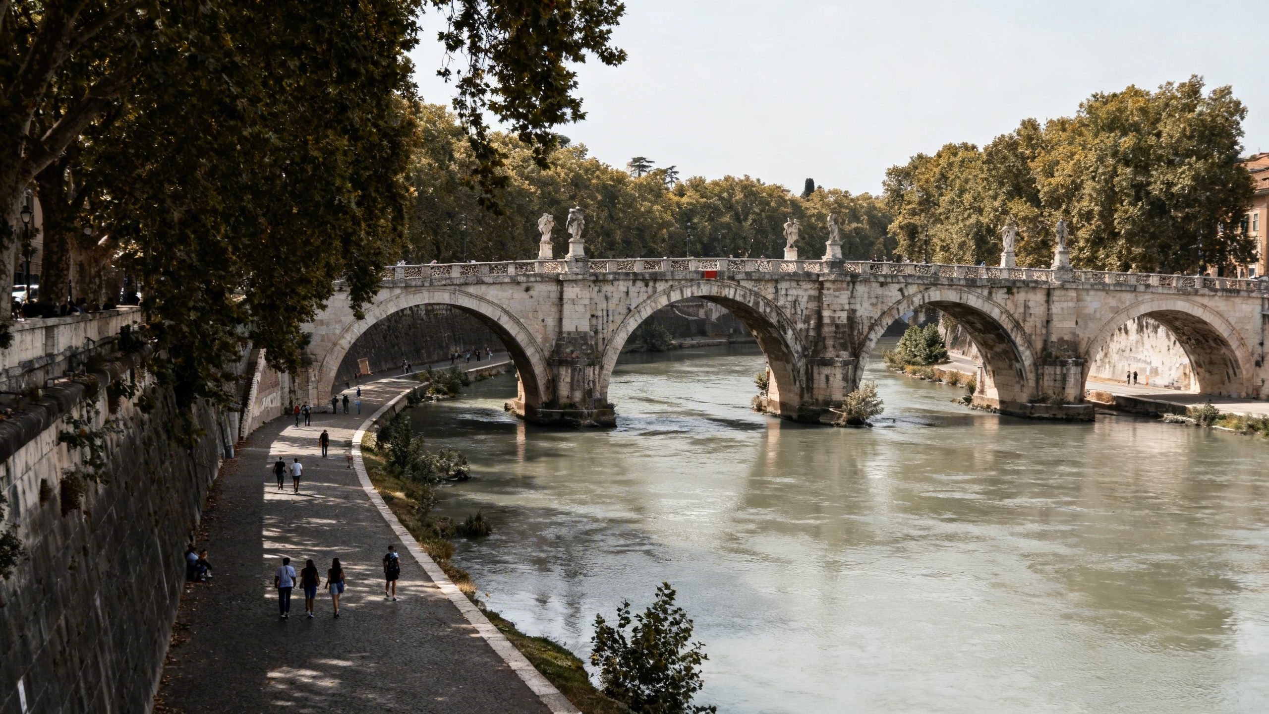 Ancient stone bridge Ponte Milvio arching over the Tiber River lined with trees and pedestrian walkways