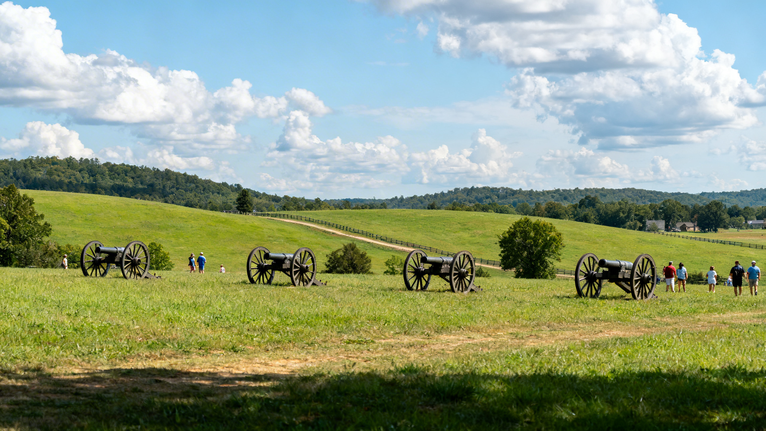 Rolling green hills and historic cannons dotting the battlefield fields with blue skies and fluffy clouds overhead