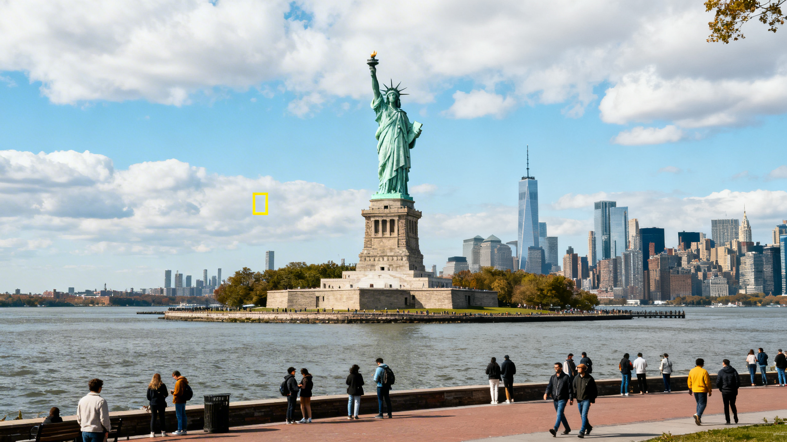 The Statue of Liberty standing tall on Liberty Island with the Manhattan skyline in the background under a partly cloudy sky