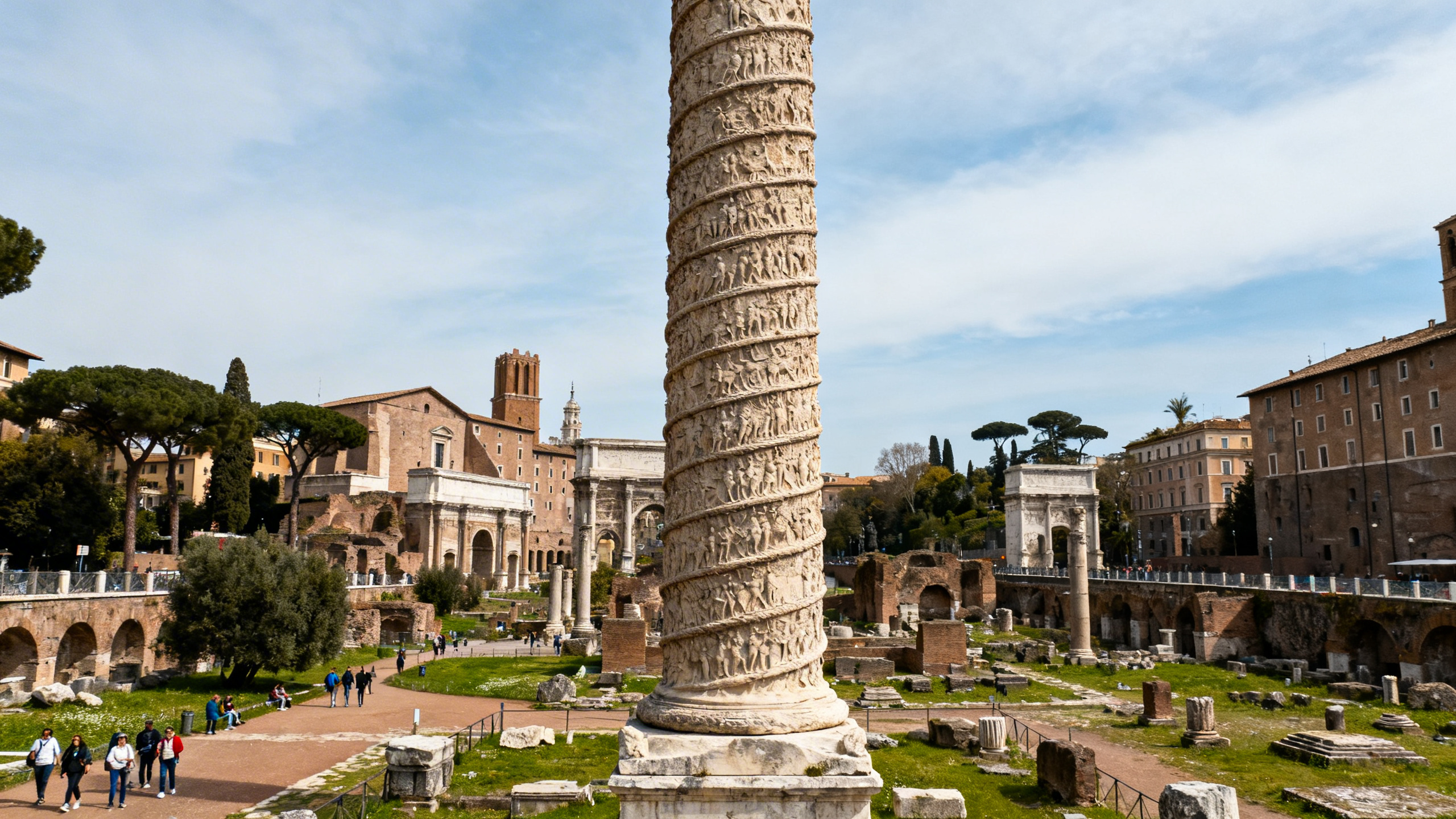 The tall, intricately carved spiral column standing in Trajan’s Forum with ancient ruins and tourists nearby