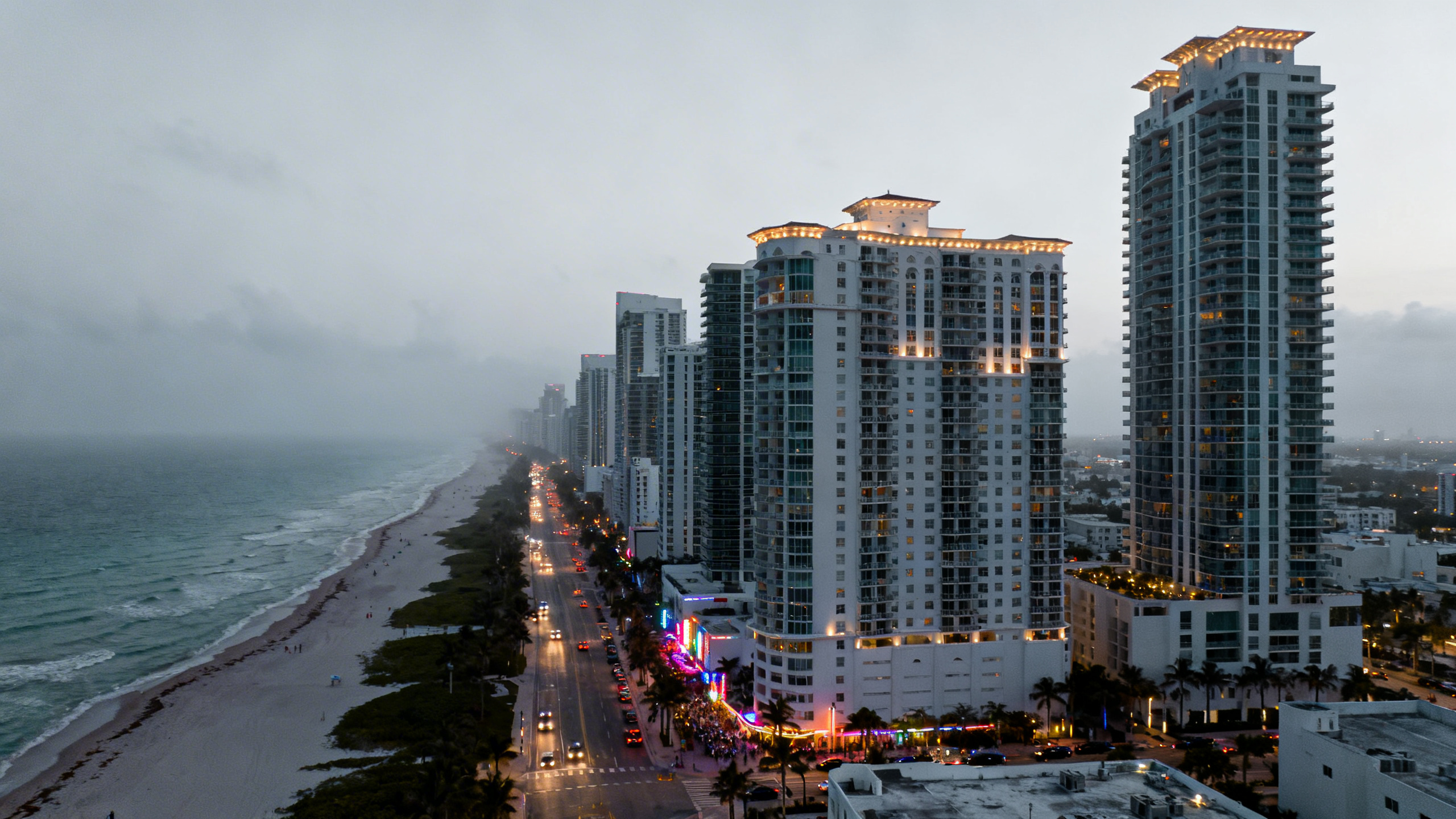 Beachfront high-rise condos and bustling Miami streets with vibrant nightlife nearby under evening lights.