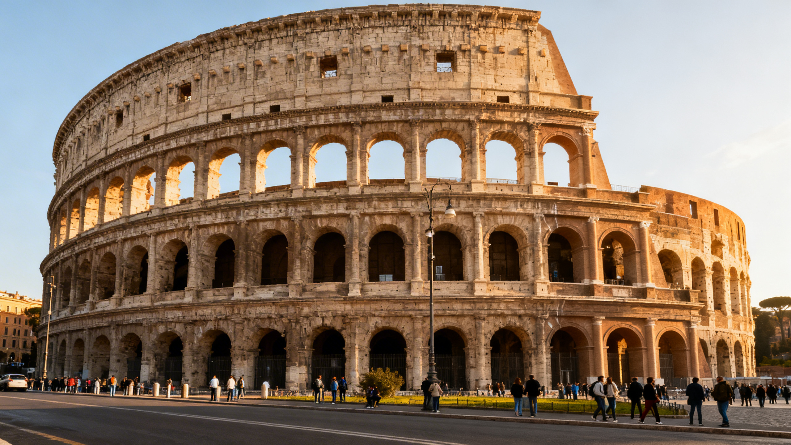 The massive, elliptical stone and concrete structure of the Colosseum bathed in afternoon sunlight with tourists gathered nearby