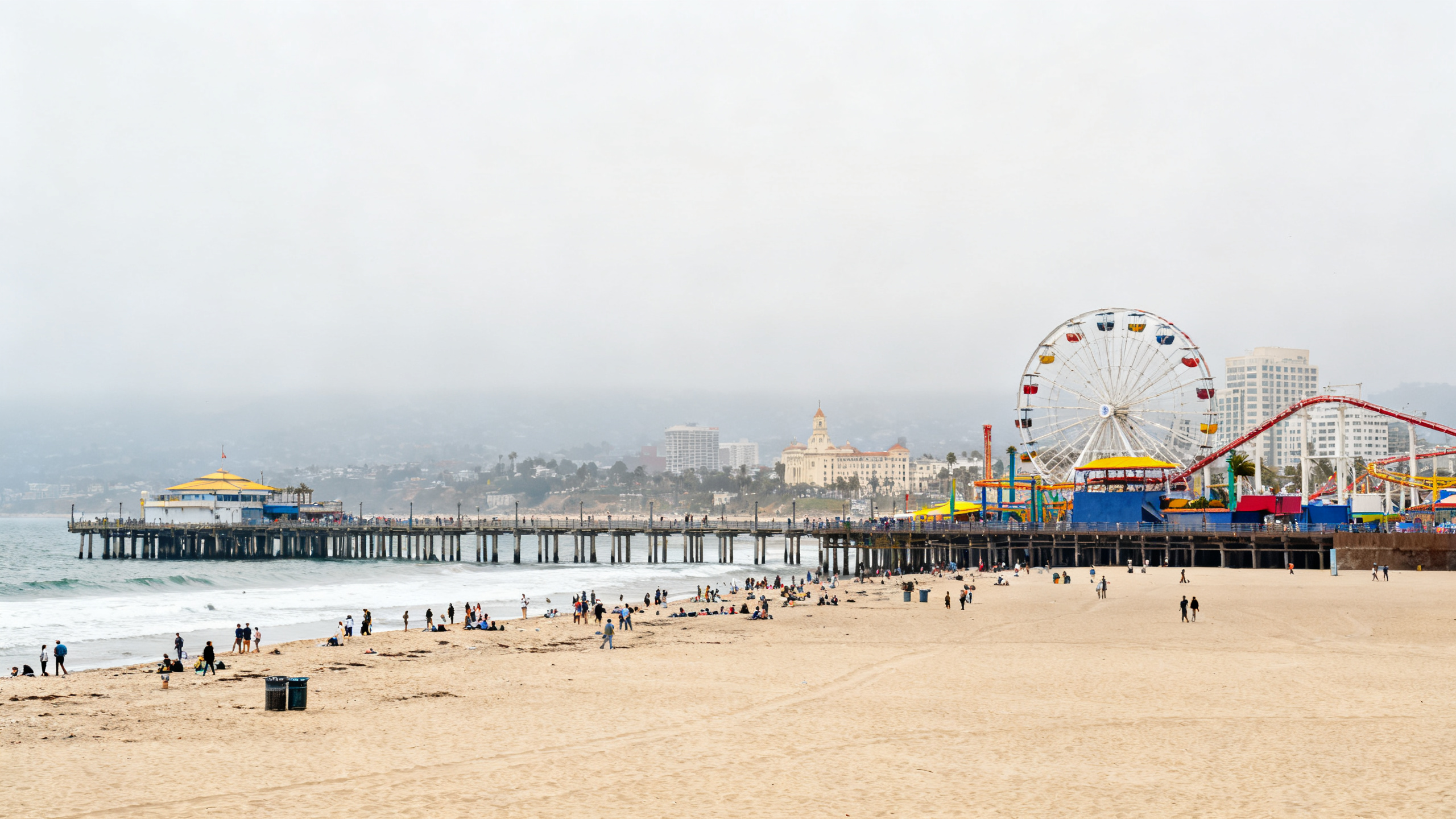 Busy beachfront with colorful amusement park rides and packed sandy shores along Santa Monica Pier