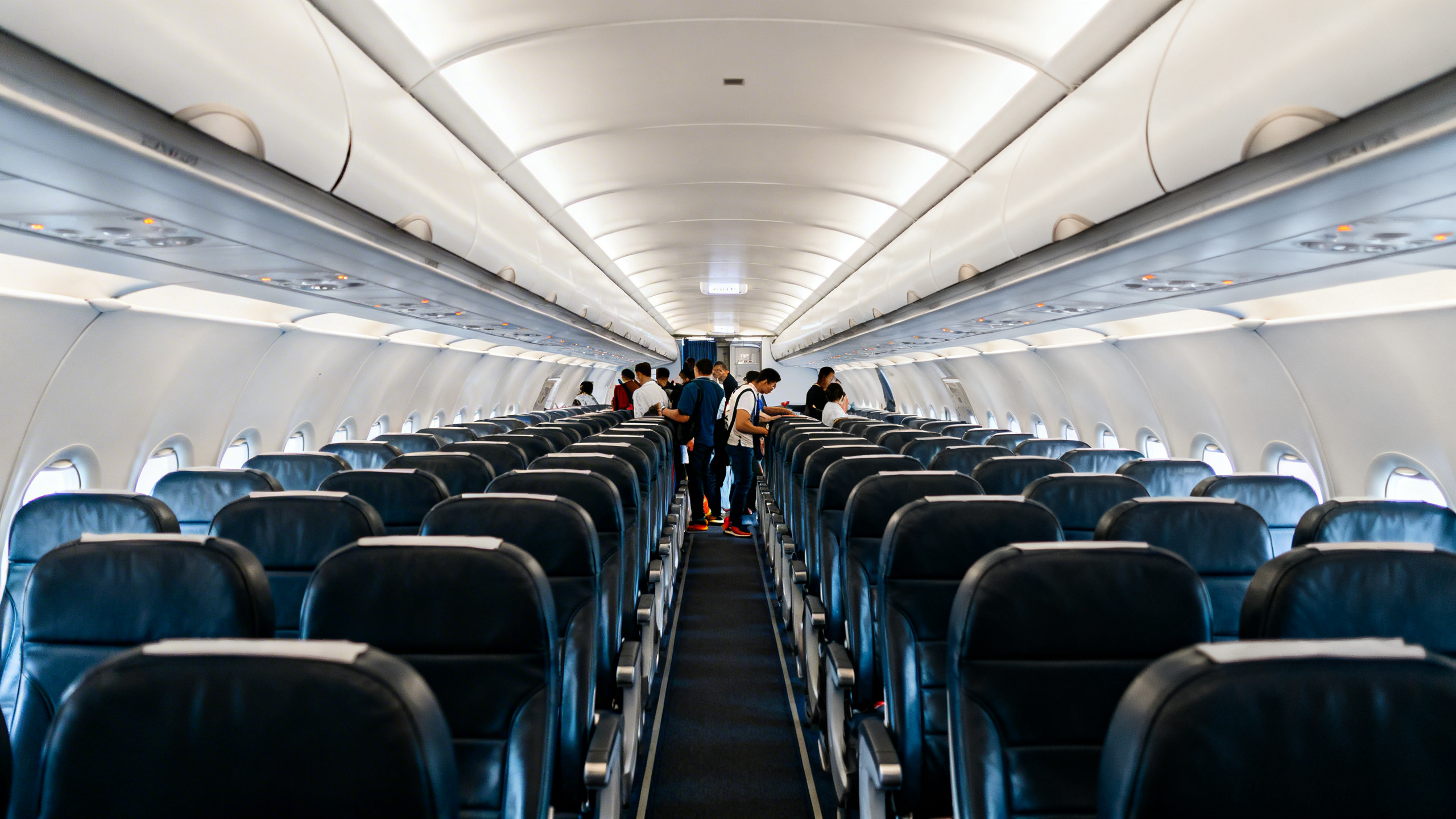 Airplane cabin interior showing rows of economy seats near the front with passengers boarding