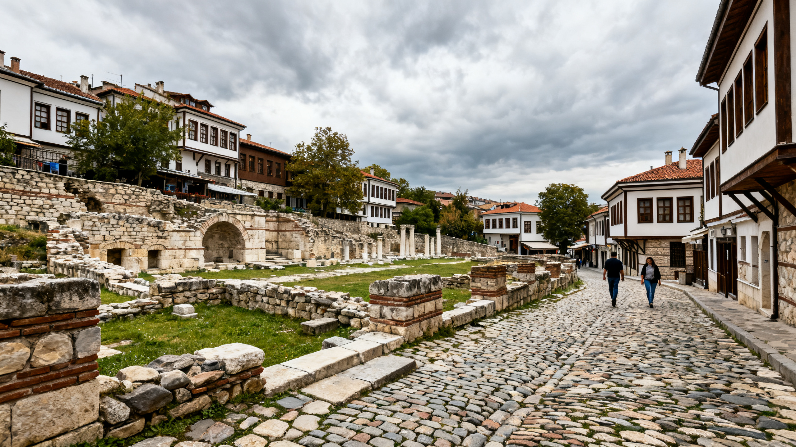Historic street in Plovdiv’s Old Town, with ancient ruins and cobblestones under a cloudy sky, visitors strolling nearby