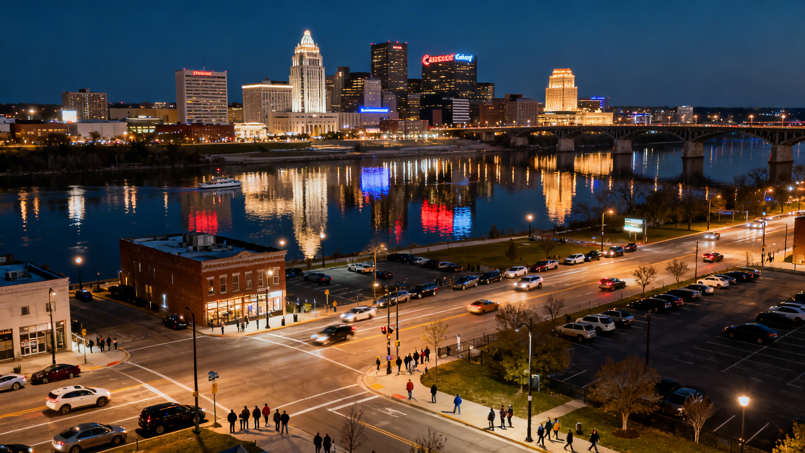 Nighttime view of the illuminated Kansas City skyline reflecting on the Missouri River, with busy urban streets below