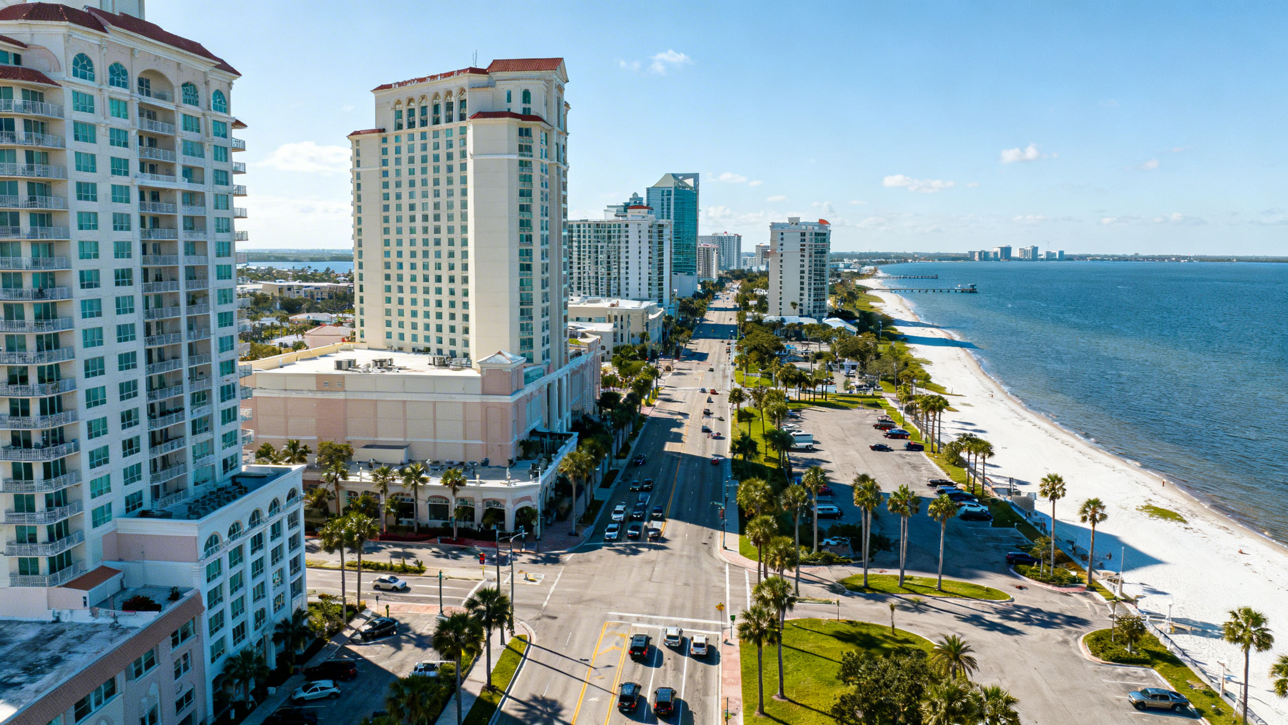 Coastal cityscape of Tampa with large hotels and condos along a sunny shoreline, with busy streets and palm-lined avenues.