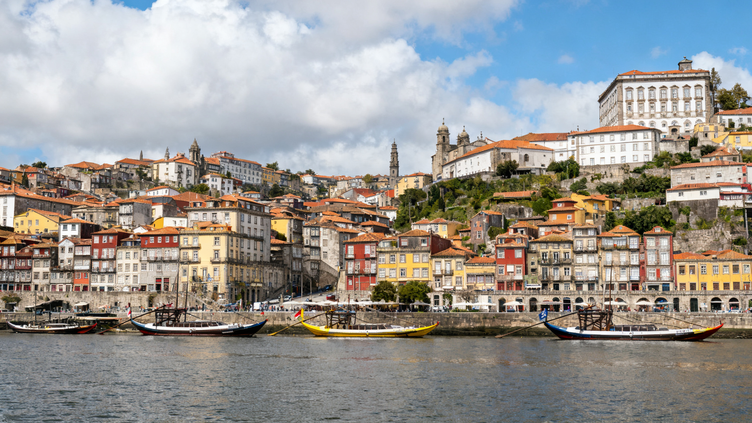 Historic riverside district with colorful multi-story buildings and boats moored on the Douro River under a partly cloudy sky
