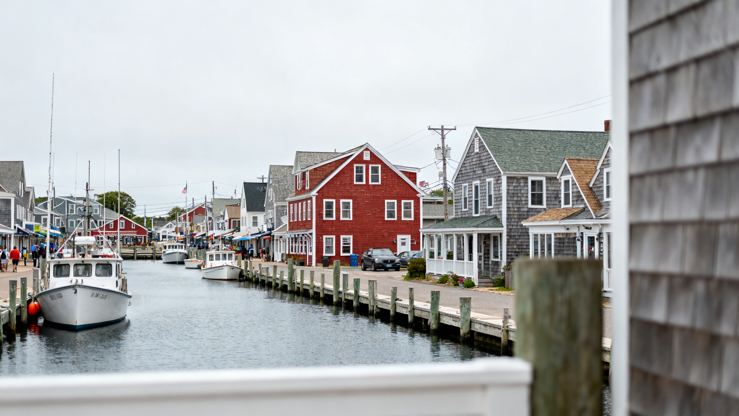 Classic Cape Cod seaside town with colorful shingled cottages and boats docked along a bustling harbor street.