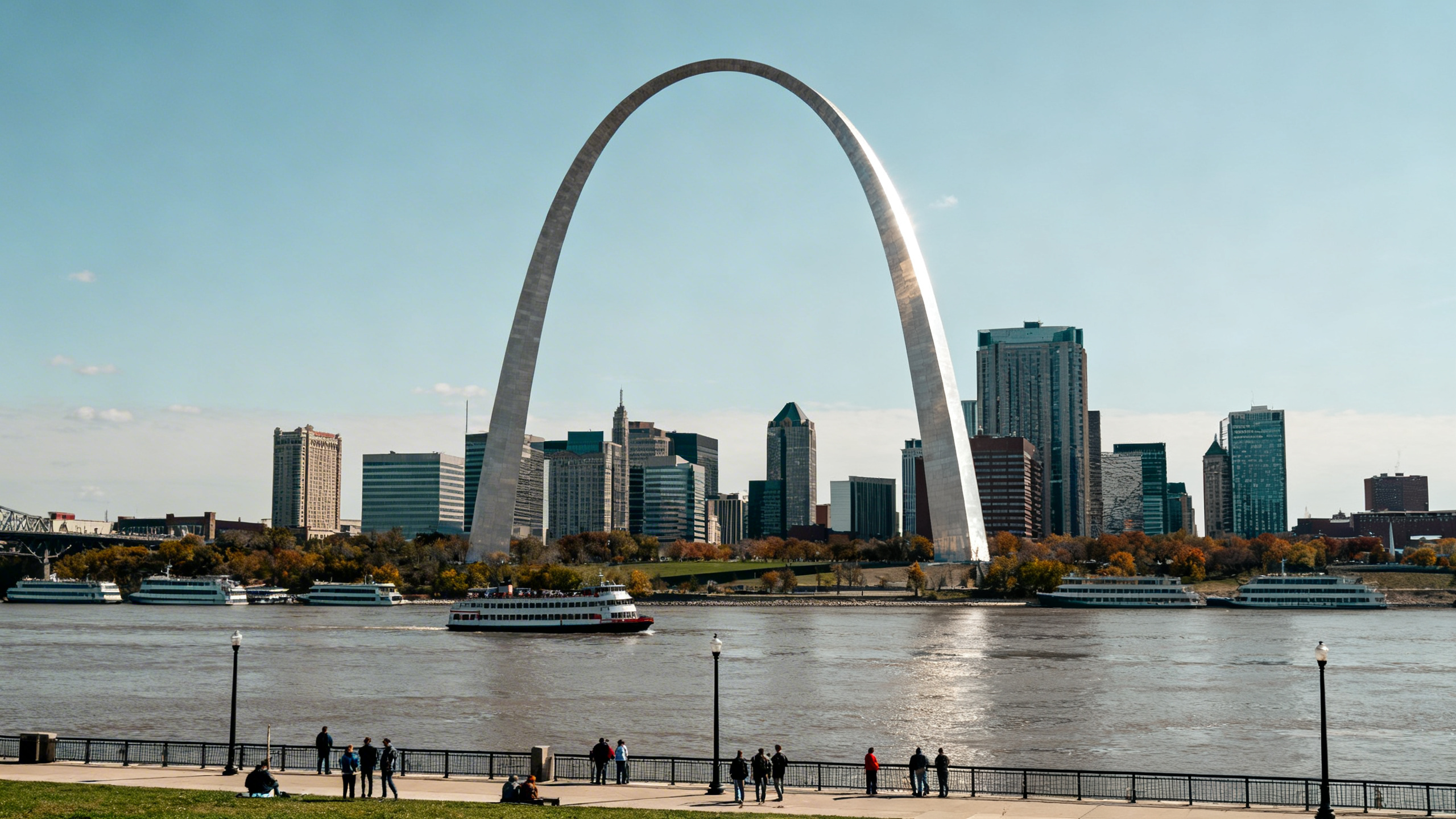 The gleaming silver Gateway Arch soaring above the Mississippi River surrounded by cityscape and river traffic