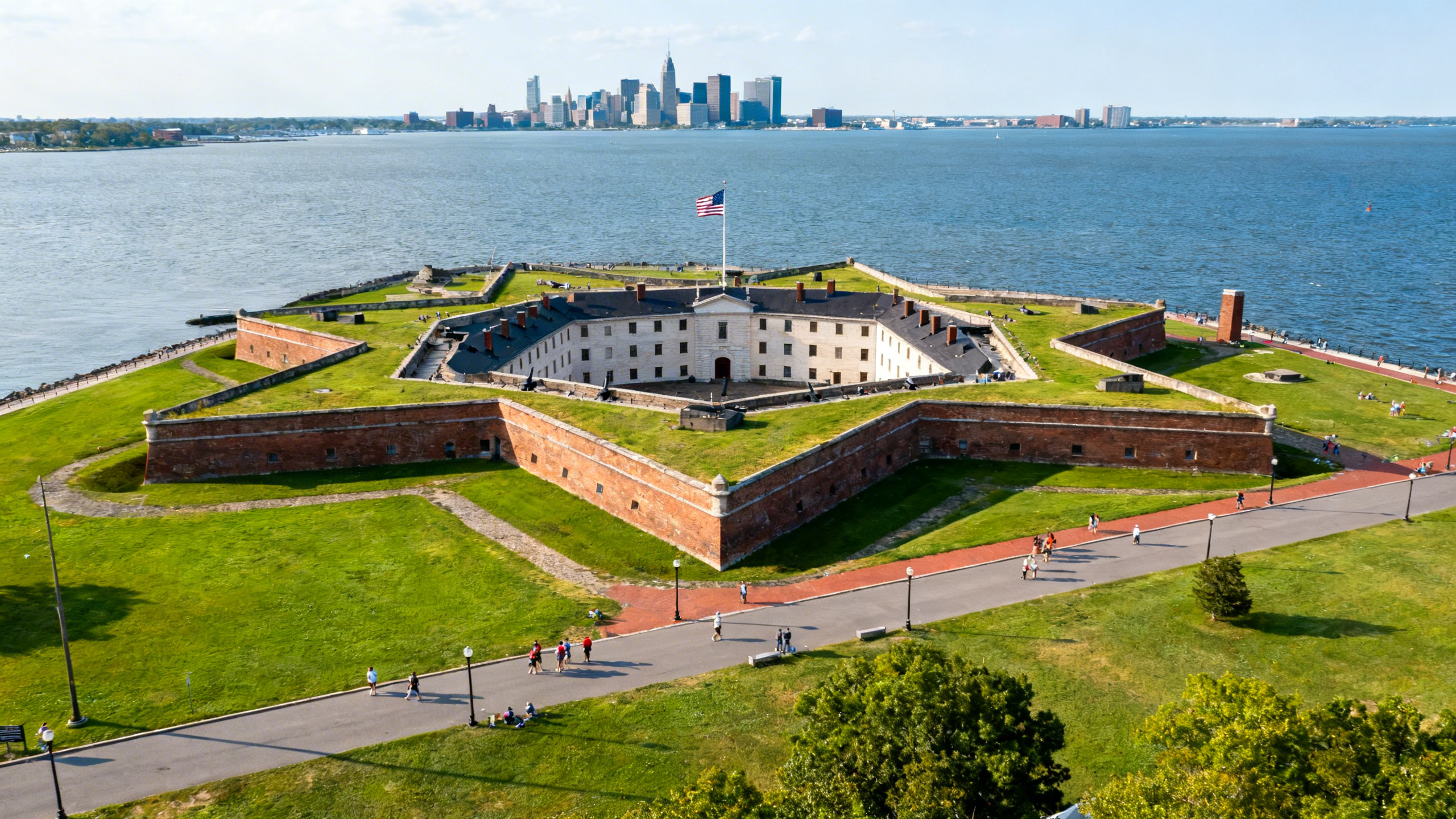 The star-shaped Fort McHenry surrounded by water and green lawns with the city skyline in the distance on a bright day