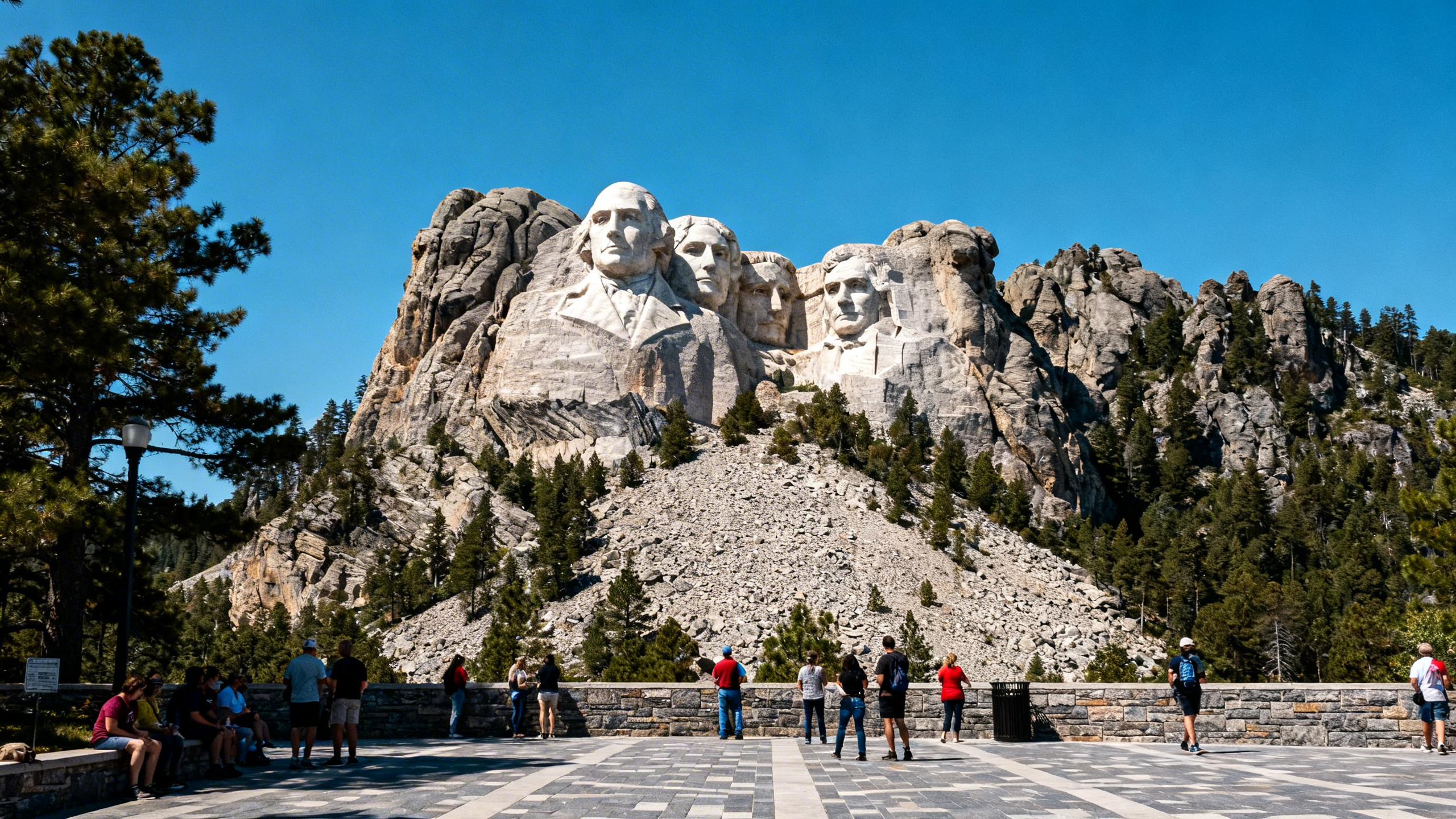 The massive carved faces of four U.S. presidents on Mount Rushmore, set against a clear blue sky and forested hills